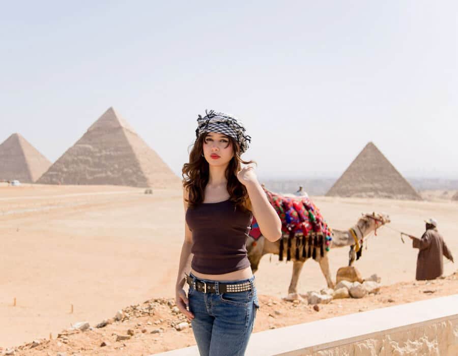Stylish girl posing with a camel in the desert, with the Pyramids of Giza backdrop in Egypt.