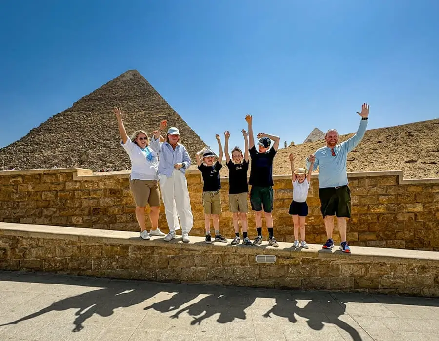 A happy family of tourists cheering in front of the Great Pyramid of Giza during an Egypt family tour.