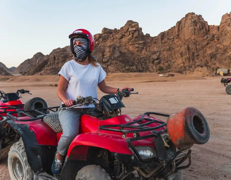 A tourist on a red quad bike adventure during a desert safari trip in Egypt with rocky mountains.