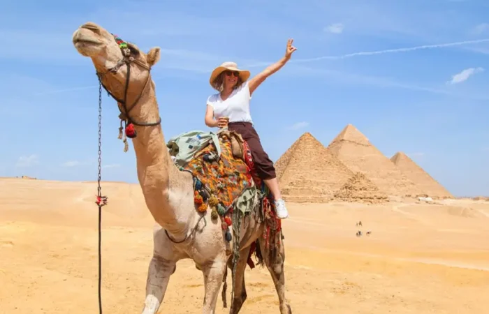 Tourist riding a camel making a peace sign in front of the Great Pyramids of Giza in Egypt.