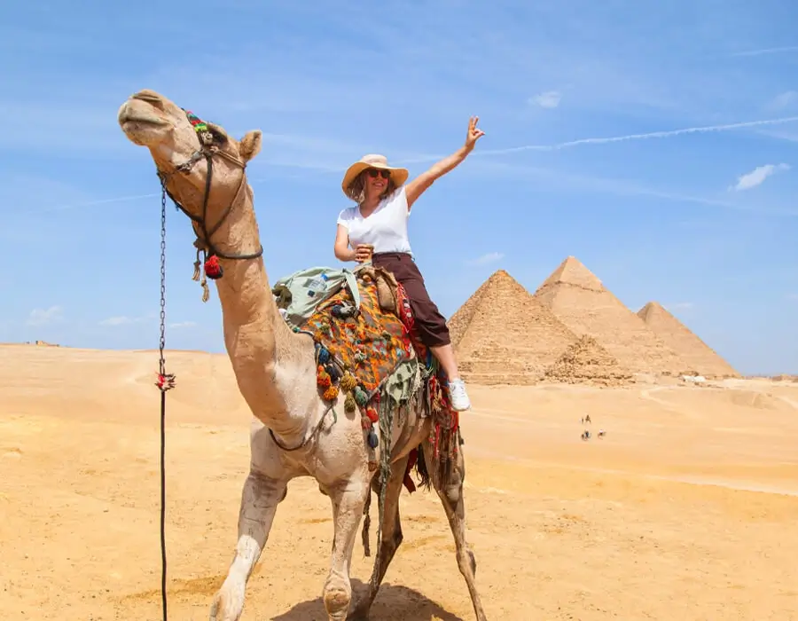 Tourist riding a camel making a peace sign in front of the Great Pyramids of Giza in Egypt.