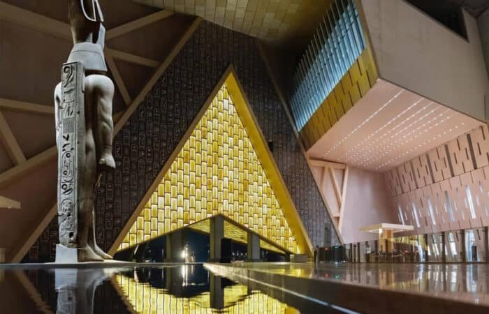 Dramatic photo of a statue and illuminated pyramidal structure inside the GEM.