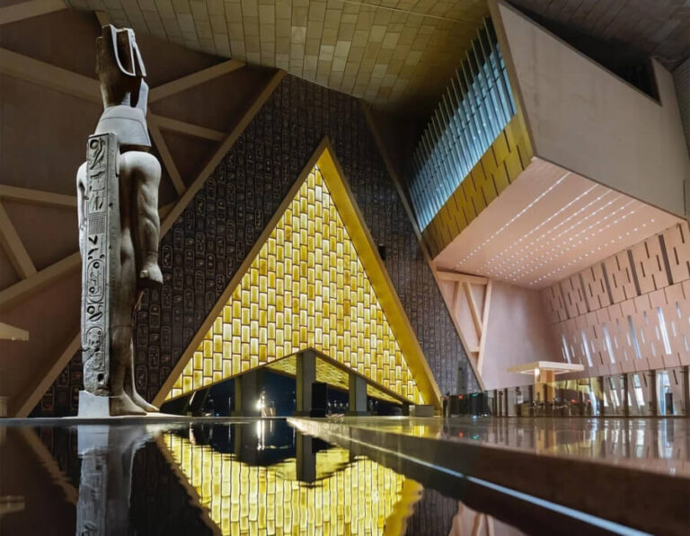 Dramatic photo of a statue and illuminated pyramidal structure inside the GEM.
