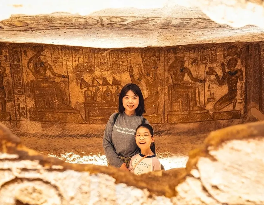 Mother and daughter on a family trip exploring ancient Egyptian temple carvings and hieroglyphics.