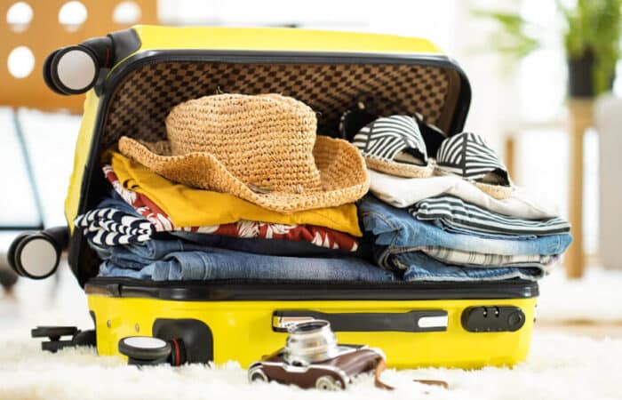 Open yellow suitcase filled with clothes, a straw hat, and sandals on a soft surface.